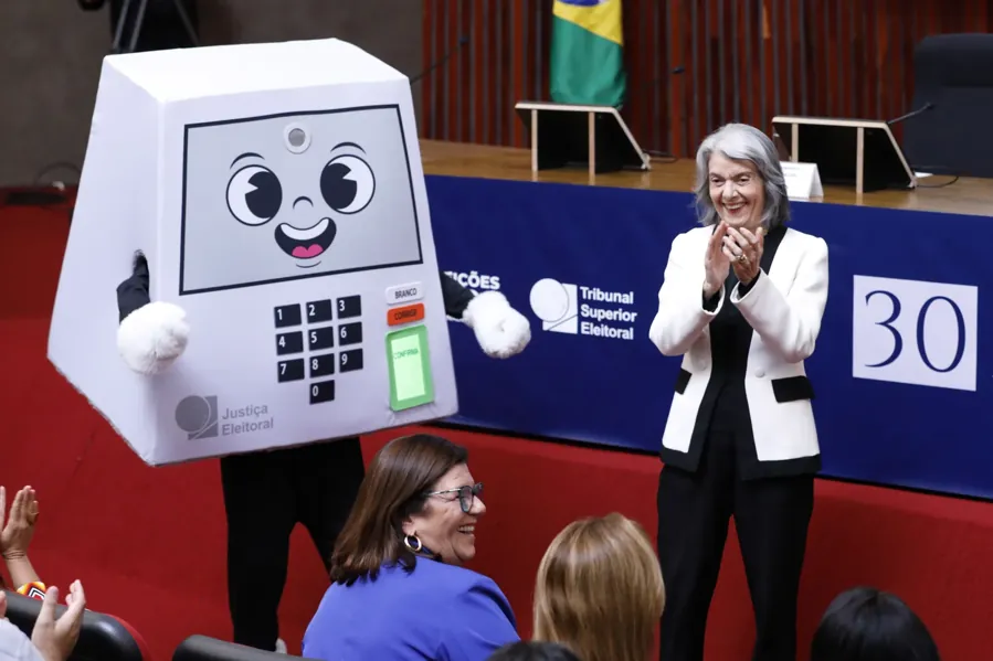 A mascote da urna na cerimônia dos 30 anos da urna eletrônica, no TSE, com a ministra Cármen Lúcia. Foto: Alejandro Zambrana / Secom / TSE, via Wikimedia Commons, domínio público